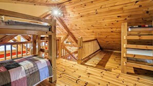 L’intérieur d’un chalet en bois, avec un lit superposé, une couverture matelassée et un escalier en bois.