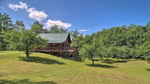 Une cabane en bois avec un toit en métal, entourée d’une zone herbeuse et d’arbres.