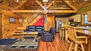 L’intérieur d’une cabane en rondins, avec un escalier en bois, un salon doté de meubles en cuir et une cuisine avec des armoires en bois.