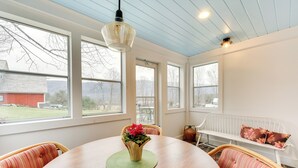 A dining area with a round wooden table, wicker chairs, and a bench with floral cushions. - Manchester Center Home w/ Green Mtn Views! (Manchester Center)