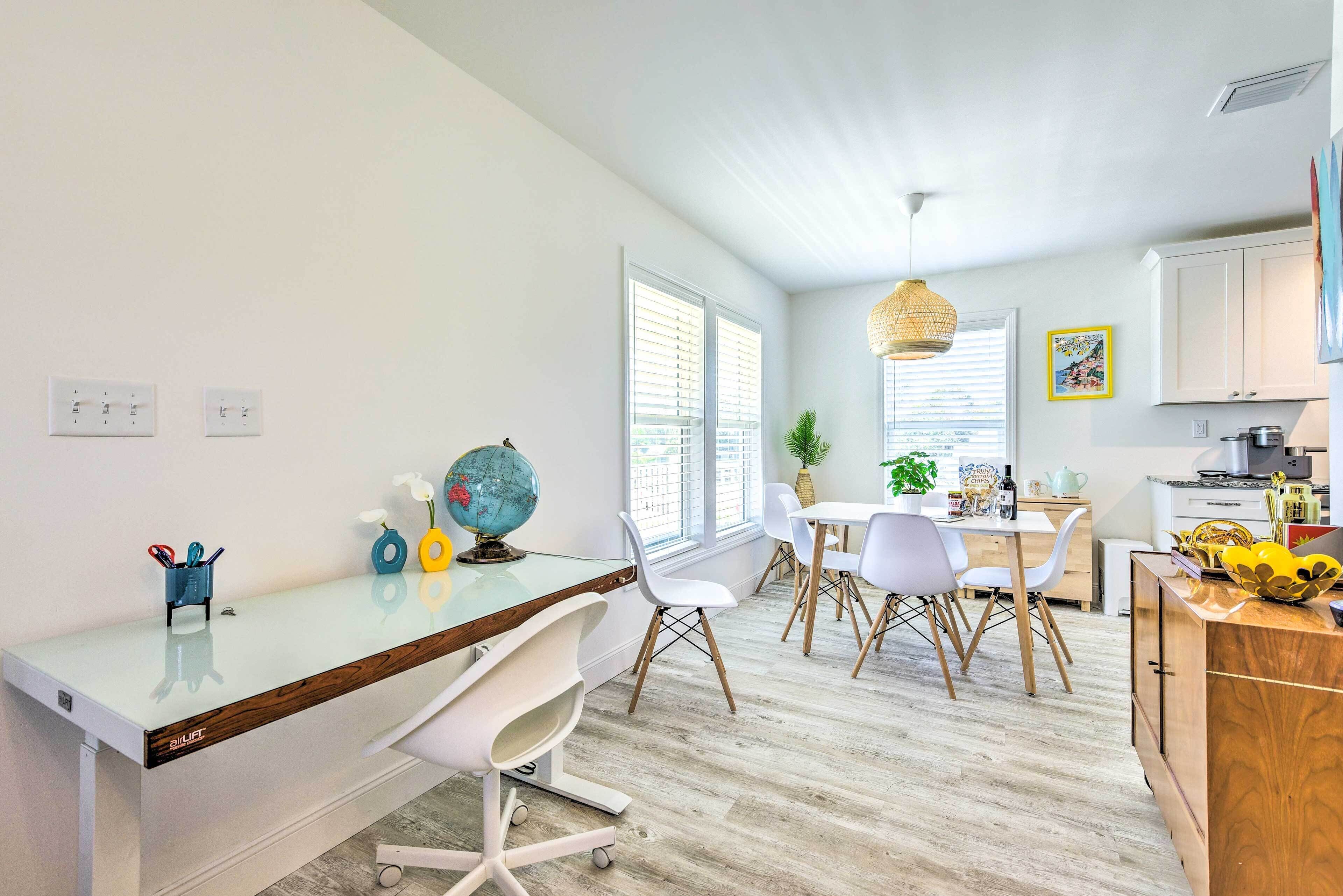 A modern kitchen with white cabinets, a dining area with white chairs, and a large window with blinds.