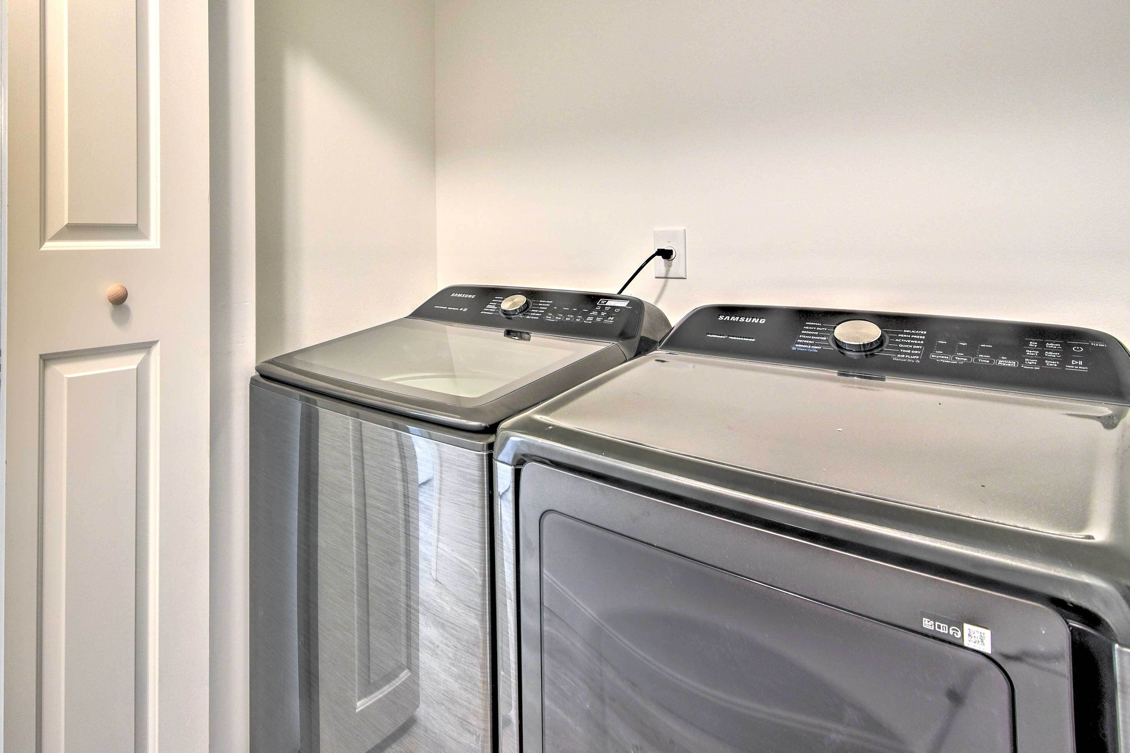 A laundry room with two stacked washers and dryers, a white door, and a wall-mounted electrical outlet.