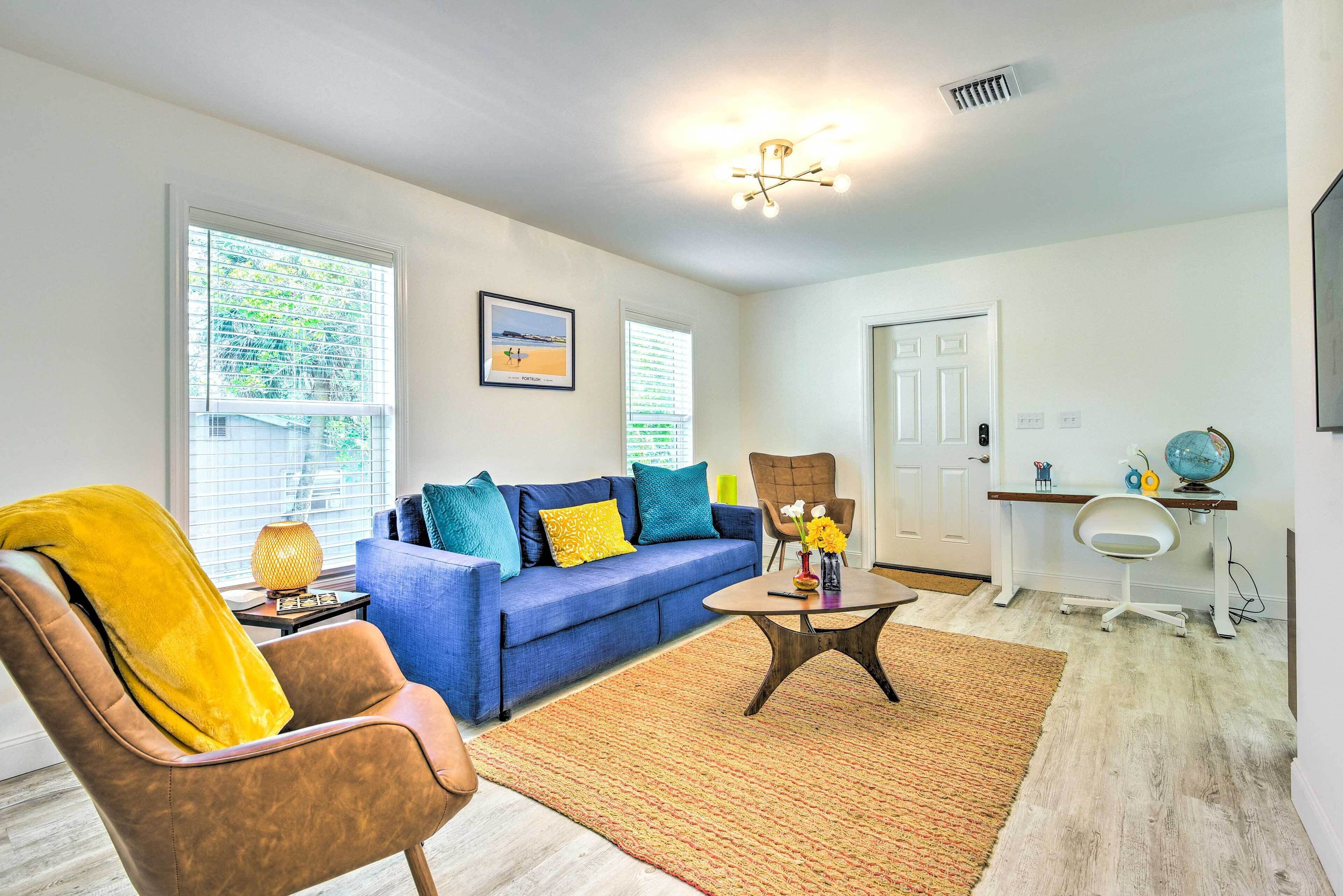 A living room with a blue sofa, a brown armchair, a coffee table, and a dining area with a white chair and a small table.