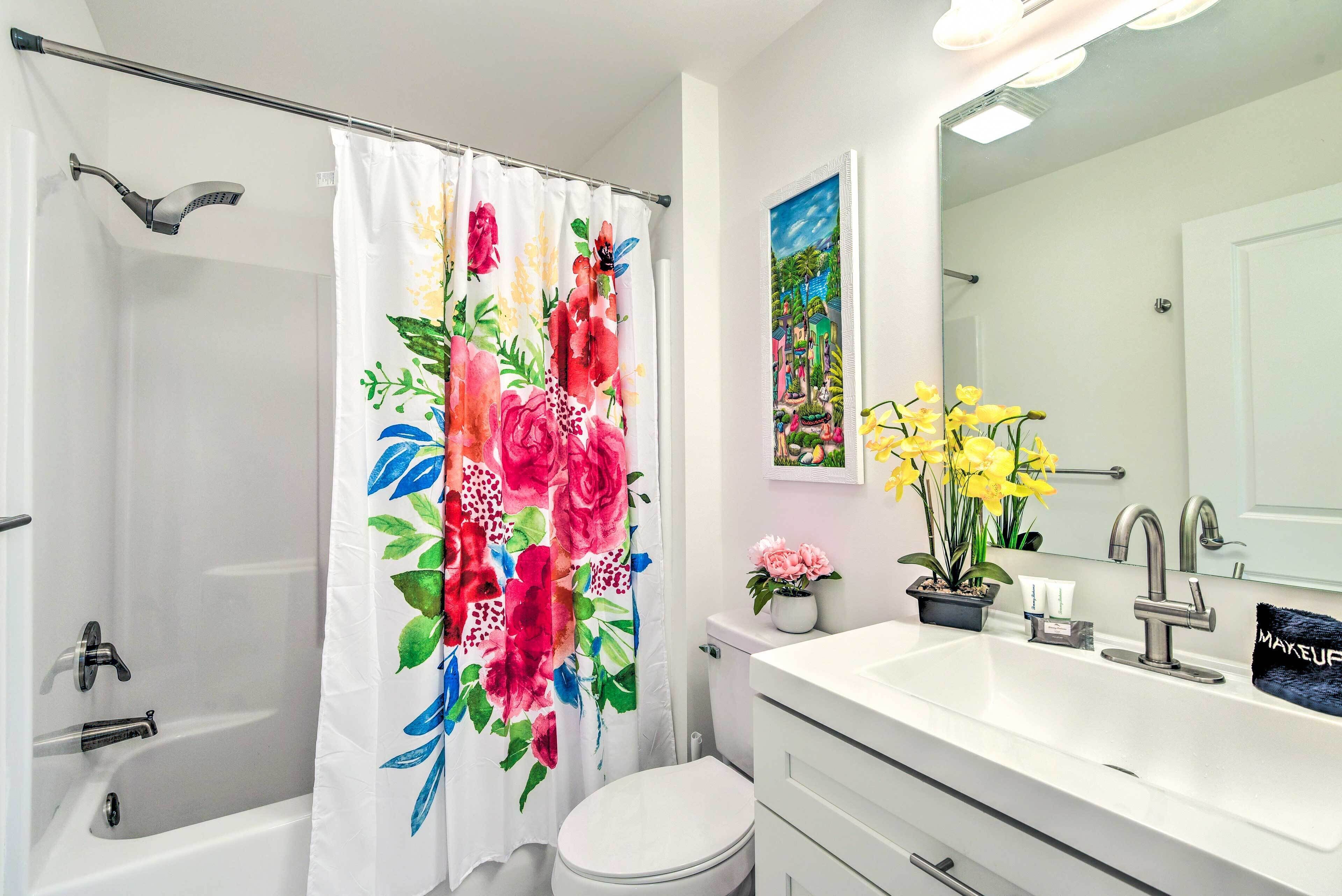 A bathroom with a shower, toilet, sink, and a mirror with a floral painting.