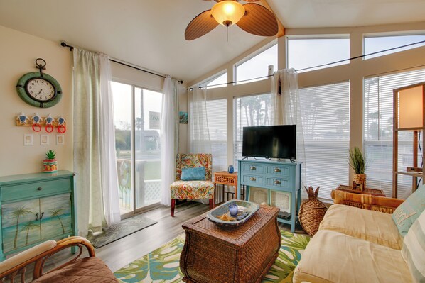 A living room with a television, a wicker coffee table, a sofa, and a chair. - Furnished Deck: Waterfront Port Isabel Cottage! (Port Isabel)