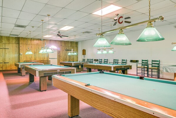 A pool hall with multiple pool tables, green lamps, and wooden paneling on the walls.