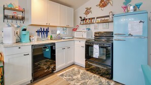 A kitchen with white cabinets, a blue refrigerator, a microwave, and a dishwasher. There are decorative items on the walls and a rug on the floor. - Furnished Deck: Waterfront Port Isabel Cottage! (Port Isabel)