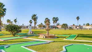 A miniature golf course with a central fountain, surrounded by palm trees and houses. - Furnished Deck: Waterfront Port Isabel Cottage! (Port Isabel)