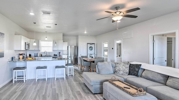 A modern kitchen with white cabinets, a central island with stools, a dining area with a table and chairs, and a living area with a sofa and ottoman. - Near Ocean: Surfside Beach Gem w/ Deck & Views! (Freeport)
