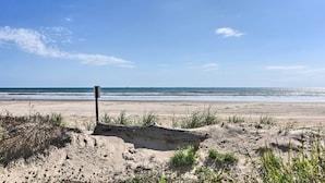 A sandy beach with a wooden post and sparse vegetation. - Near Ocean: Surfside Beach Gem w/ Deck & Views! (Freeport)