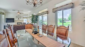 A spacious dining area with a glass table, leather chairs, a chandelier, and a view of the outdoors. - 2 Mi to Coachella: Indio Home w/ Fire Pit! (Indio)