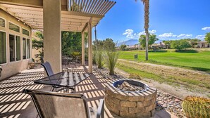 A covered patio with outdoor furniture, a fire pit, and a view of a well-maintained lawn and distant mountains. - 2 Mi to Coachella: Indio Home w/ Fire Pit! (Indio)