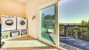A laundry area with two washing machines, a drying rack, and a glass door leading to a balcony with a view of the ocean.