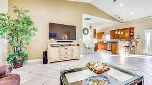 A spacious living room with a large flat-screen TV, a glass coffee table with seafood, a potted plant, and a leather sofa.