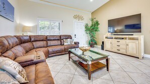 A living room with a sectional sofa, a glass coffee table, a TV on a wooden cabinet, and a door with a window.