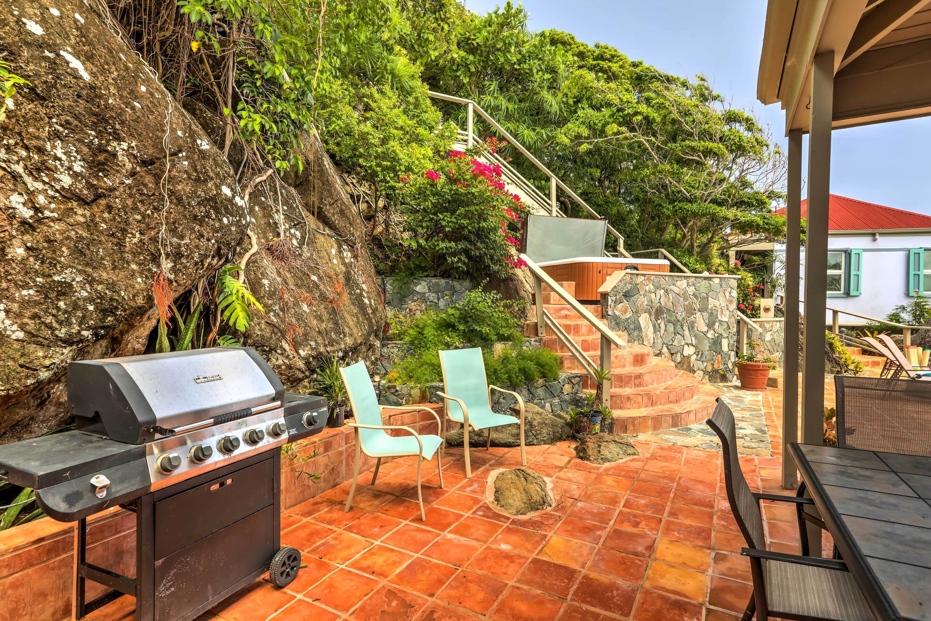 Une terrasse extérieure équipée d’un barbecue, de deux chaises, d’une table et d’un escalier menant à une maison.