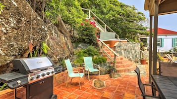 Une terrasse extérieure équipée d’un barbecue, de deux chaises, d’une table et d’un escalier menant à une maison.