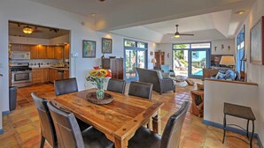 A spacious dining area with a wooden table and chairs, a kitchen with wooden cabinets, and a view of the outdoors through large windows. - St Thomas Cliffside Villa With Pool & Hot Tub! (St. Thomas)