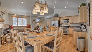 A spacious kitchen with wooden cabinets, a dining area with a wooden table set for four, and a large window providing natural light. - 5 Mi to Ski Resort: Breck Home w/ Hot Tub! (Breckenridge)