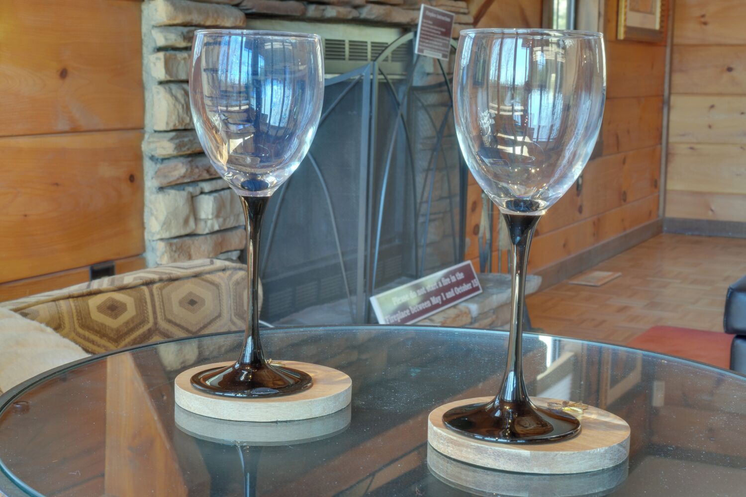Deux verres à vin vides sont posés sur une table en verre, devant un mur de pierre et un panneau d’affichage en arrière-plan.