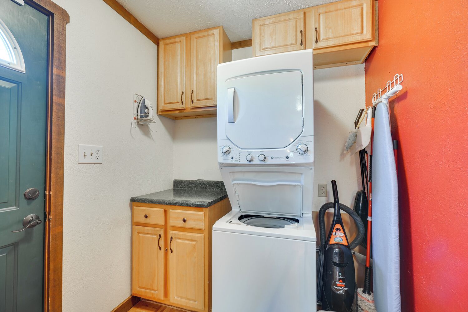 A compact kitchen with wooden cabinets, a built-in washer and dryer, and a vacuum cleaner.