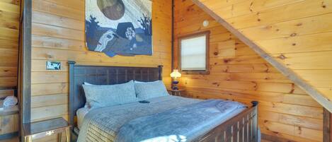 Une chambre dans un chalet en bois, avec un lit, une table de chevet, une lampe fixée au mur et une grande tapisserie.