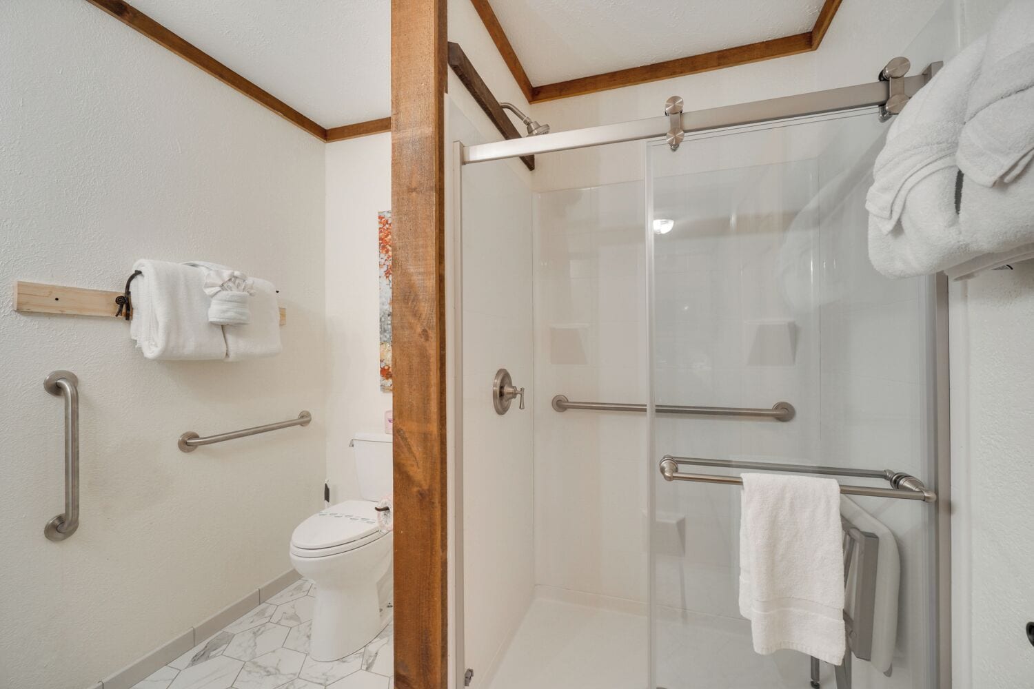 A modern bathroom with a glass shower enclosure, a toilet, and handrails.