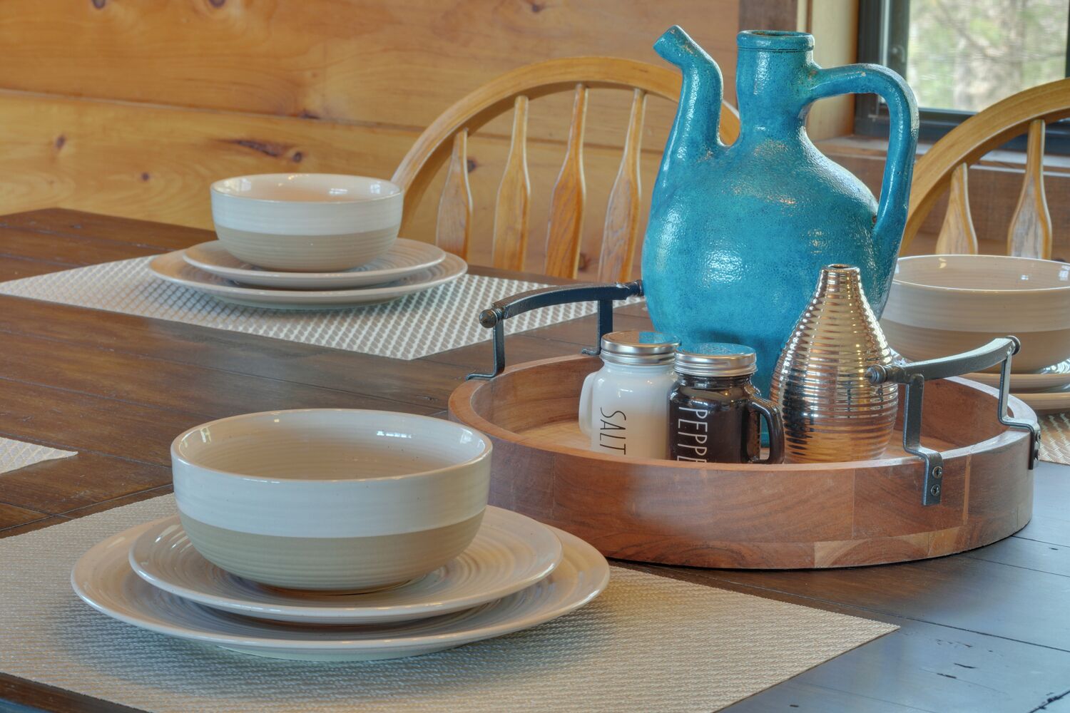 A wooden table with a set of white bowls and plates, a blue pitcher, and salt and pepper shakers.