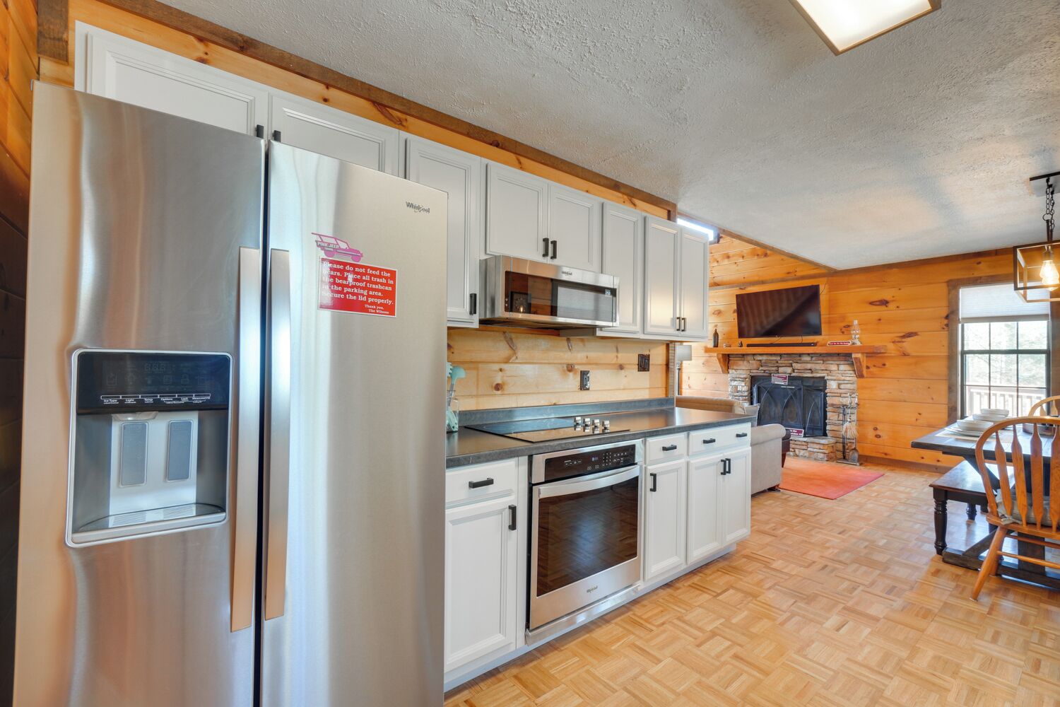 A modern kitchen with stainless steel appliances, white cabinetry, a built-in microwave, and a stone fireplace.