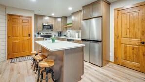A modern kitchen with wooden cabinets, stainless steel appliances, a central island with stools, and a wooden door. - 1 Block to Main St: Modern Breckenridge Condo! (Breckenridge)