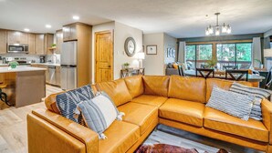 A modern kitchen with stainless steel appliances, a dining area with a wooden table and chairs, and a living room with a leather sofa and a large window. - 1 Block to Main St: Modern Breckenridge Condo! (Breckenridge)