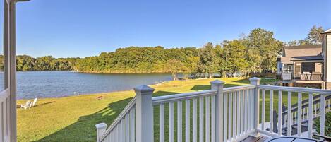 A deck with a view of a lake and a grassy area with chairs.