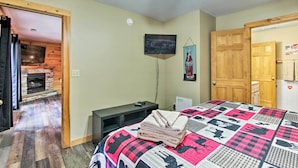 A bedroom with a bed, a television, a fireplace, and a door leading to another room.