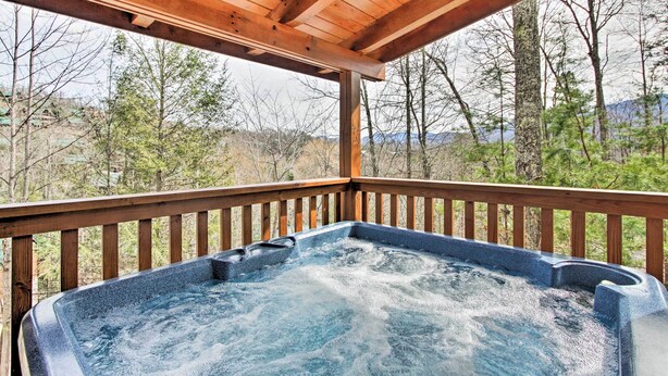 A hot tub under a wooden pergola with a view of trees and mountains.