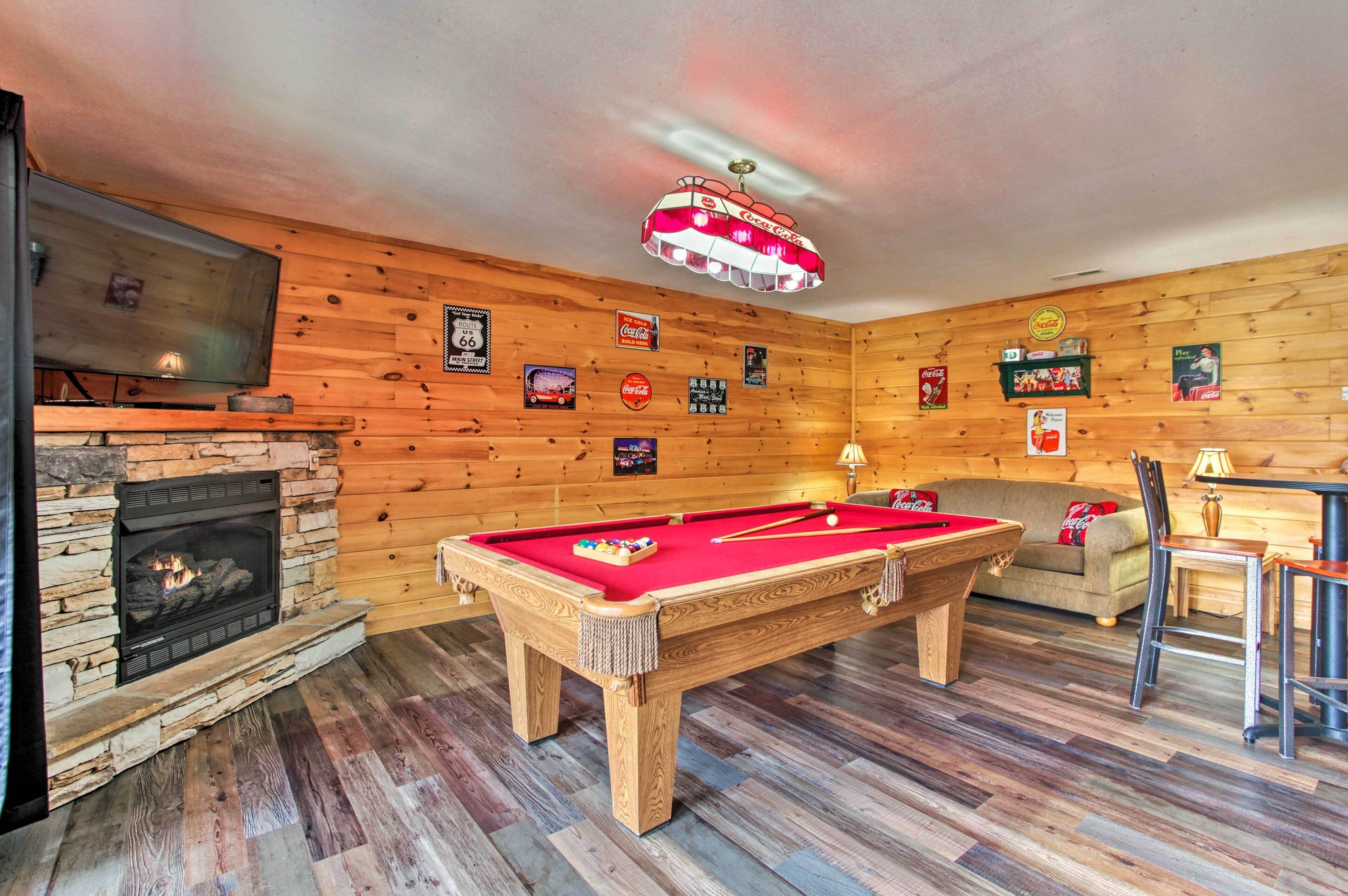 A wooden-paneled room with a pool table, a fireplace, and a television mounted on the wall.