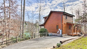 A log cabin with a stone foundation, a porch, and a paved driveway.