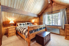 Ein Schlafzimmer einer Holzhütte mit Bett, Nachttischen, einem Schminktisch und einem Fenster mit Vorhängen, sowie einer Heizung.