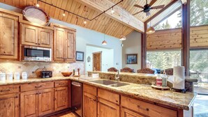 A kitchen with wooden cabinets, granite countertops, a microwave, and a large window offering a view of the outdoors. - 'one Moose Lodge' Tahoe Donner Vacation Rental! (Truckee)