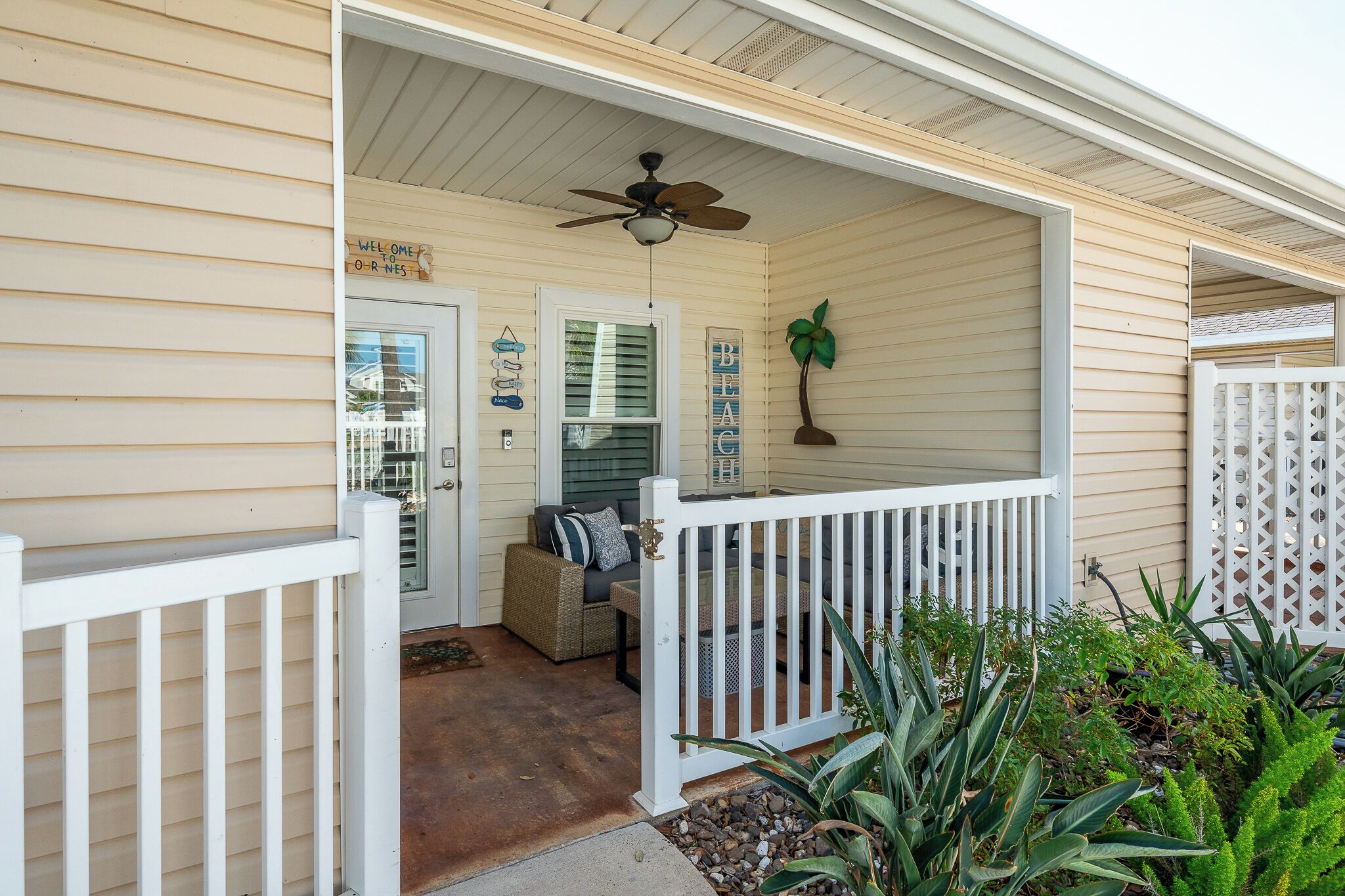 A covered porch with a ceiling fan, a white railing, and a door leading inside.