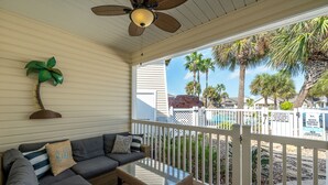 Eine überdachte Veranda mit einem Korbsessel, einem Glastisch und einem Deckenventilator.