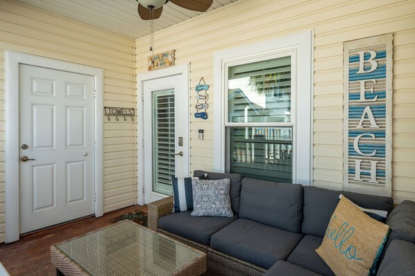 A cozy living room with a gray sofa, a wicker coffee table, and a glass door leading to the outside.