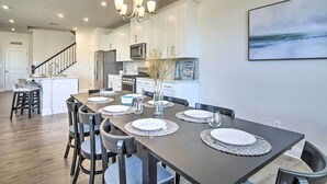 Une cuisine moderne avec des meubles blancs, une table à manger en bois foncé, dressée pour quatre personnes, et un lustre.