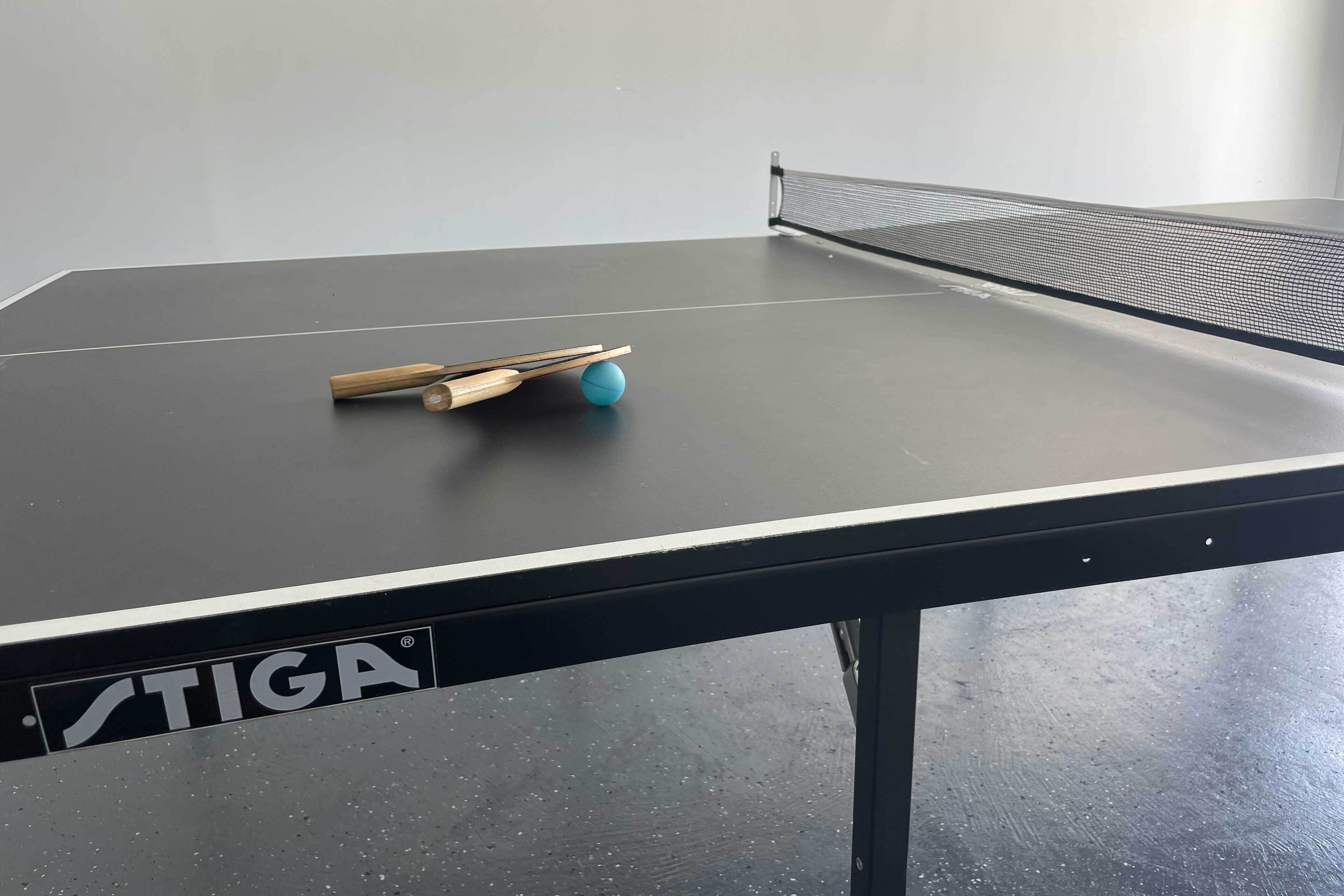 A ping pong table with a blue ball and paddles, and the brand "STIGA" visible on the table's side.