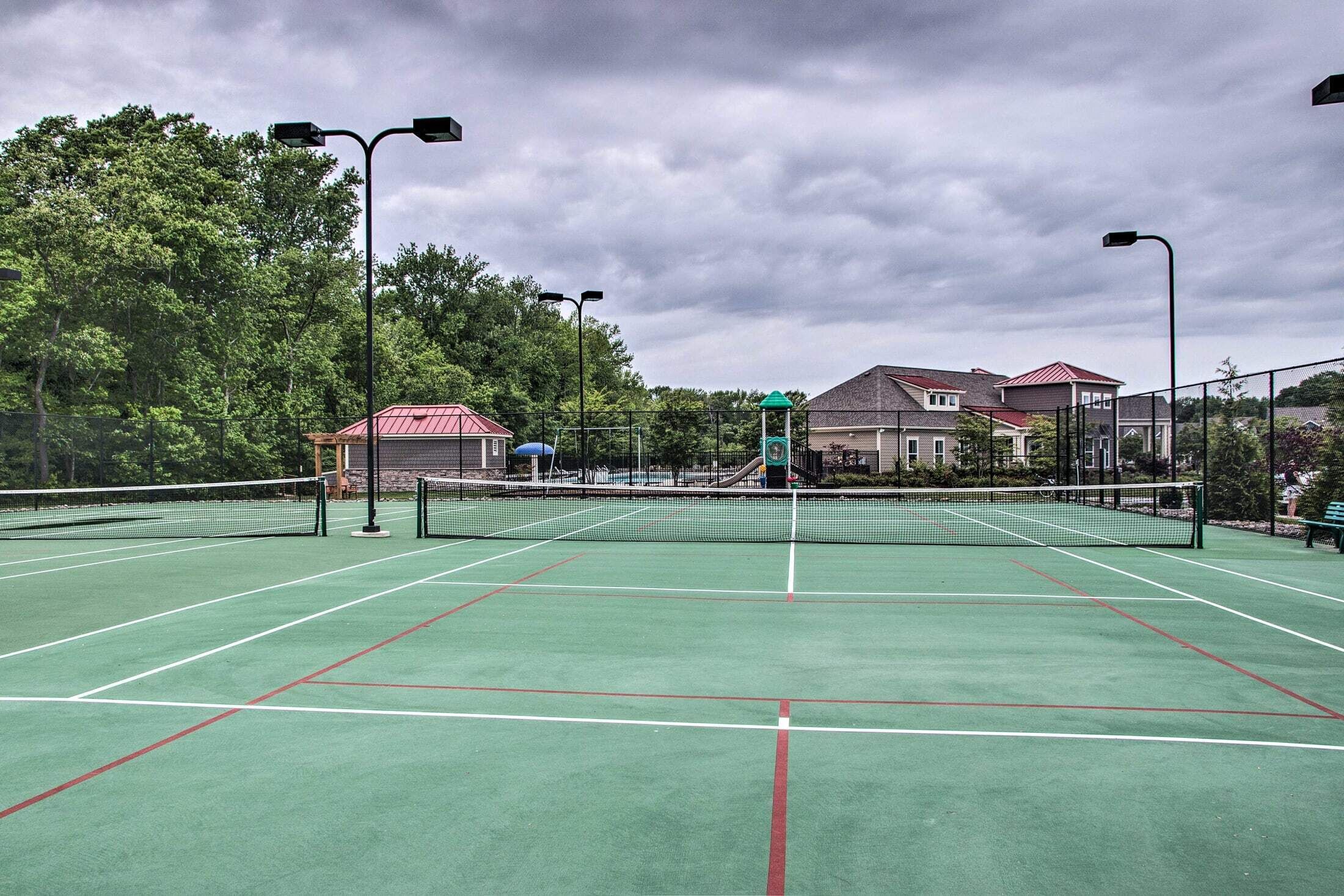 En udendørs tennisbane med net, omgivet af træer og bygninger.