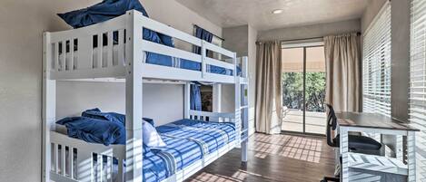 Una cama litera con ropa de cama azul, un escritorio con una silla y vista al exterior a través de una ventana.