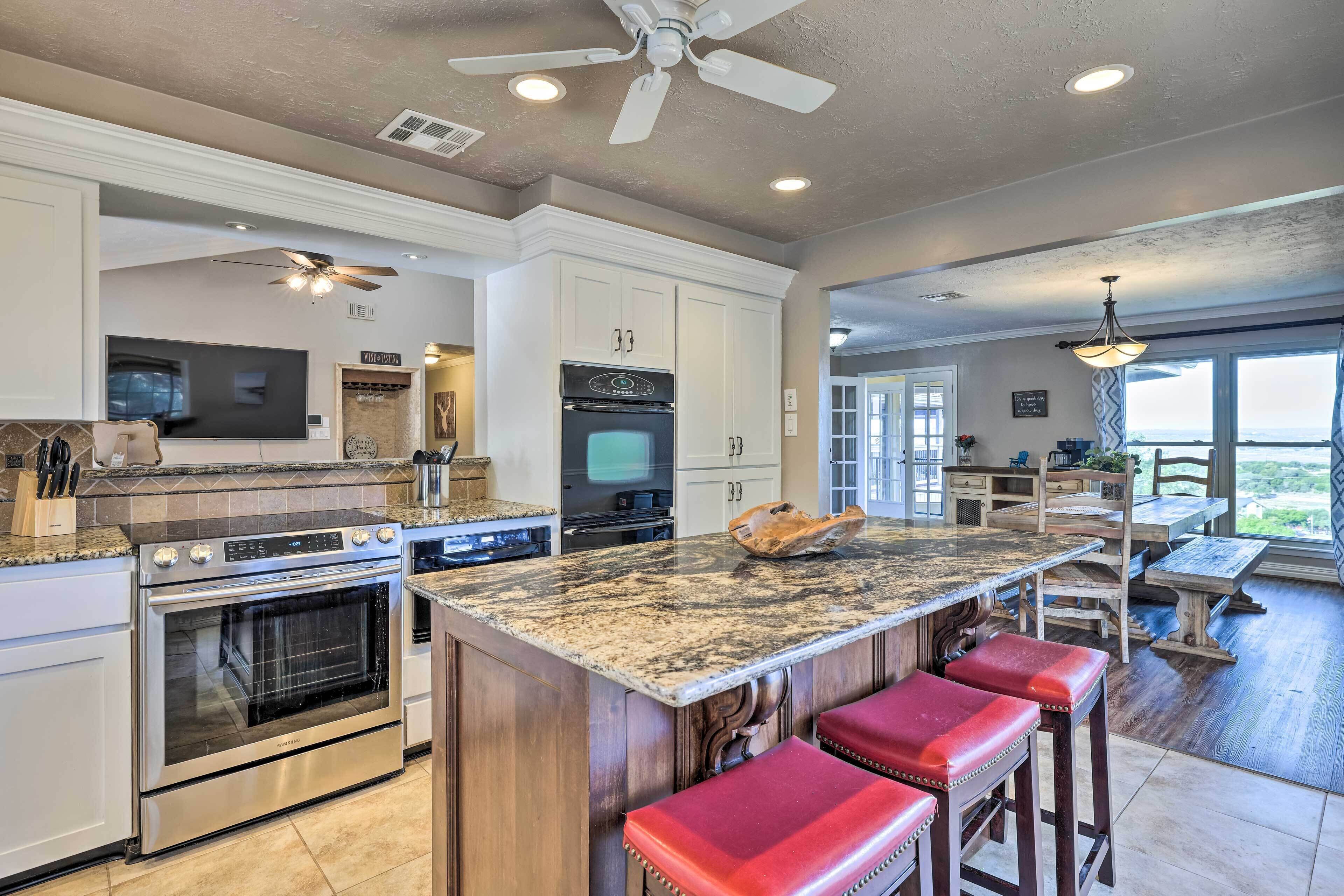 A spacious kitchen with granite countertops, stainless steel appliances, and a large island with red bar stools.