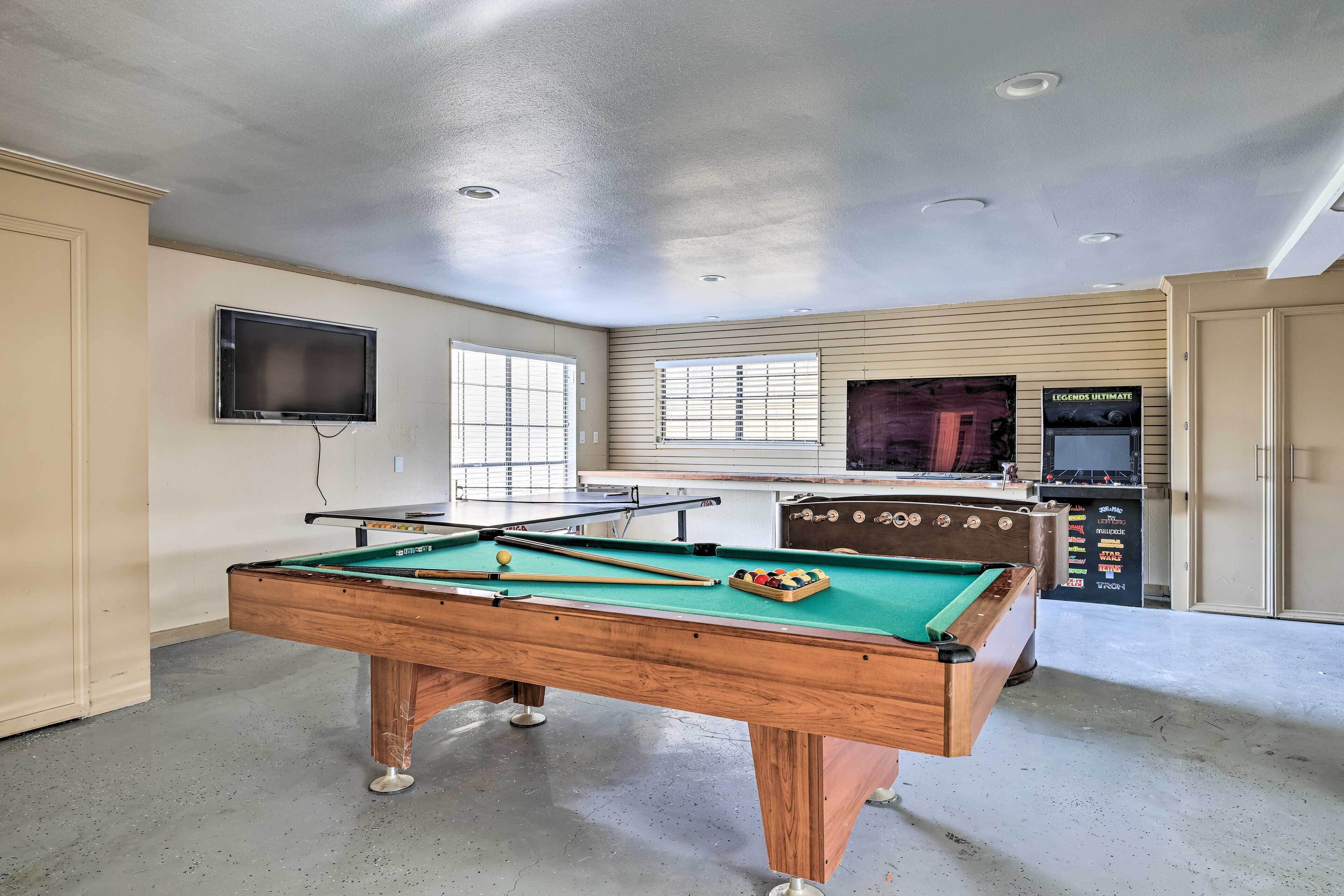 Una mesa de billar con bolas, una mesa de futbolín y un televisor montado en la pared.