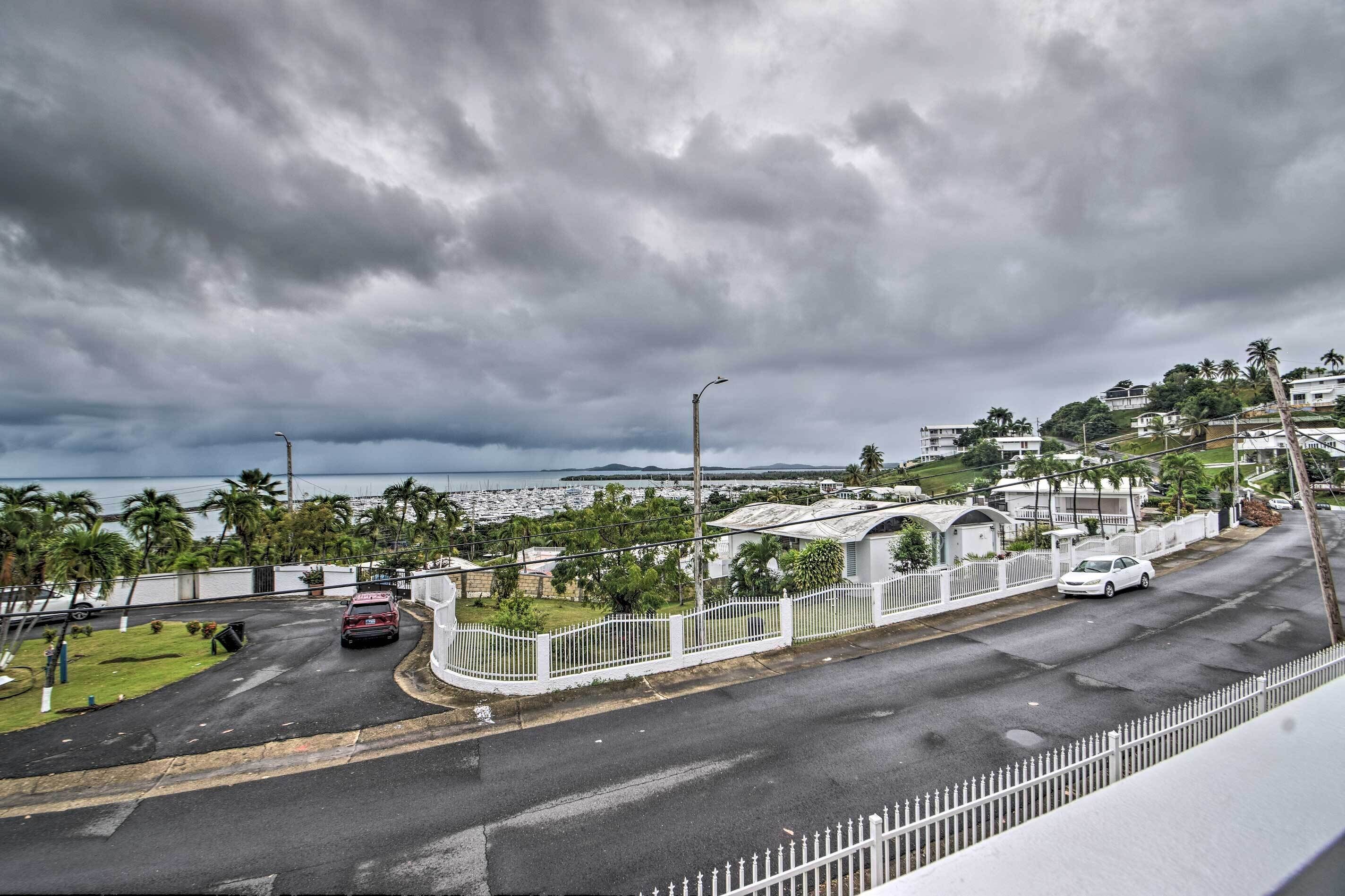 Uma estrada costeira com cerca branca, um carro vermelho e um carro branco estacionados.