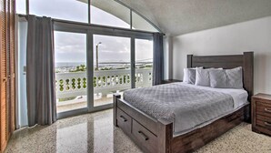 Un dormitorio con una cama grande, cabecera de madera y vista al mar a través de un ventanal corredero.