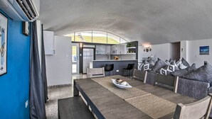 Una cocina moderna con una isla integrada, un comedor con una mesa larga y sillas, y vistas al exterior.